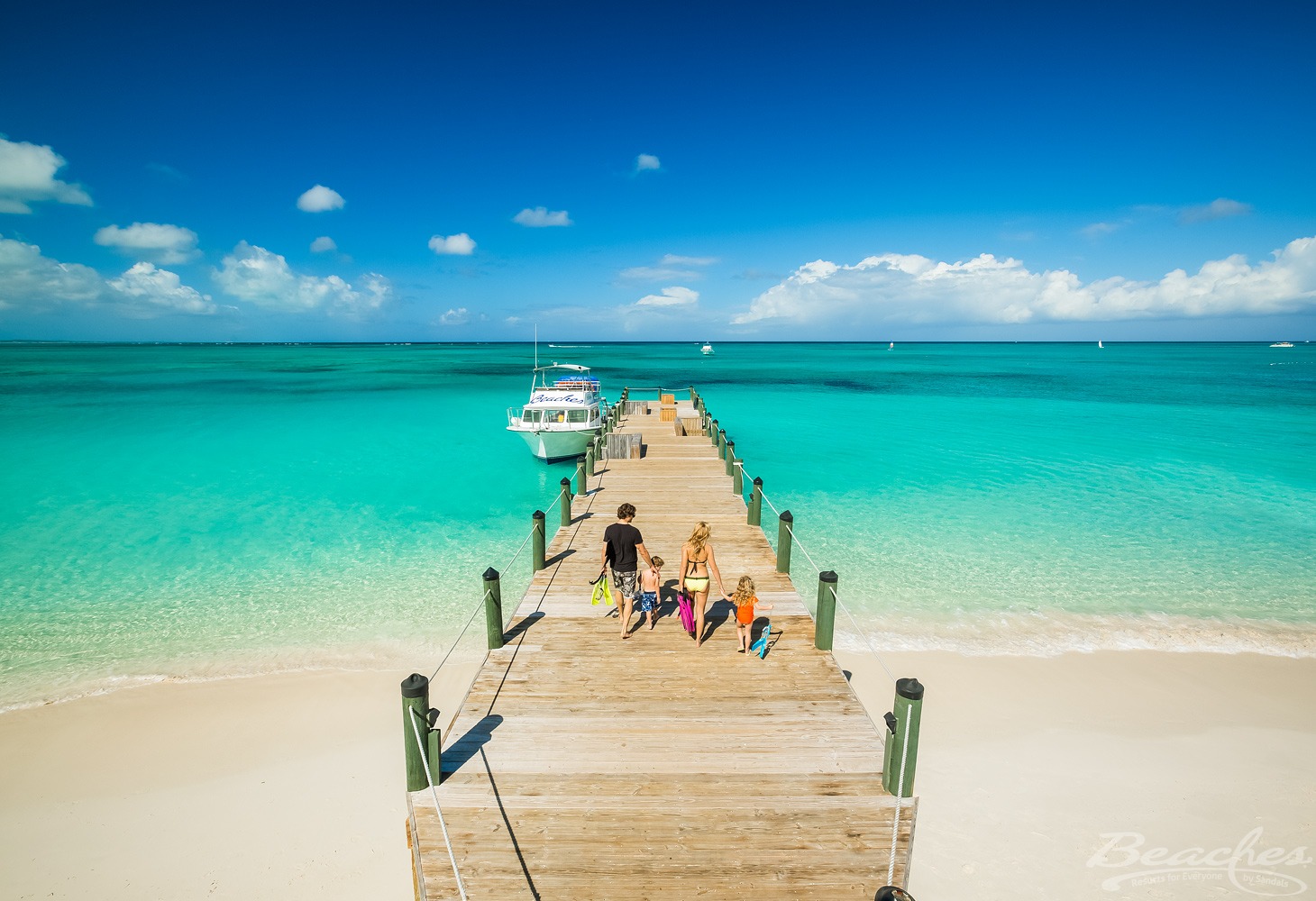 family walking along pier in turquoise water off beach